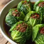 Close-up of pan-fried ground beef with soy sauce and garlic served in bright green cabbage leaves arranged on a white round plate with rustic background