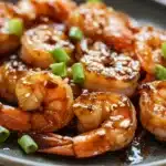 Close-up of air fryer shrimp teriyaki with a glossy sauce and sesame seeds on a clean white plate.