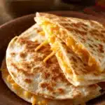 Close-up of a cheesy quesadilla with melted cheese oozing out, on a clean white plate.
