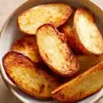 Golden-brown air fryer potato halves with crispy edges on a clean white plate