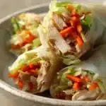 Close-up of crispy chicken spring rolls on a clean white plate with a dipping sauce.