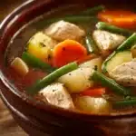 Close-up of hearty chicken vegetable soup with carrots and herbs in a white bowl.