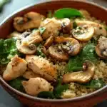 Close-up of a one pot chicken quinoa dish with mushrooms and spinach in a bright setting.