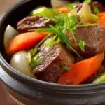 Close-up of slow cooker beef tongue with a rich, savory sauce on a white plate.