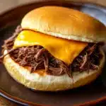 Close-up of a crock pot beef sandwich on a bun with a minimal background.