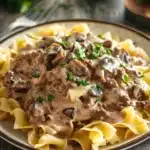 Close-up of creamy ground beef stroganoff with mushrooms and pasta on a white plate.