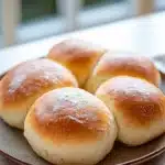 Close-up of freshly baked bread rolls on a wooden surface with a warm, inviting glow.