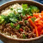 Close-up of a high protein beef and rice bowl with fresh vegetables and herbs.