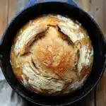 Close-up of golden no knead bread in a cast iron dutch oven with a crispy crust.