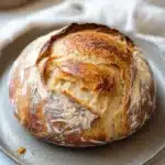 Close-up of a golden-brown no knead bread with a crispy crust on a clean background.