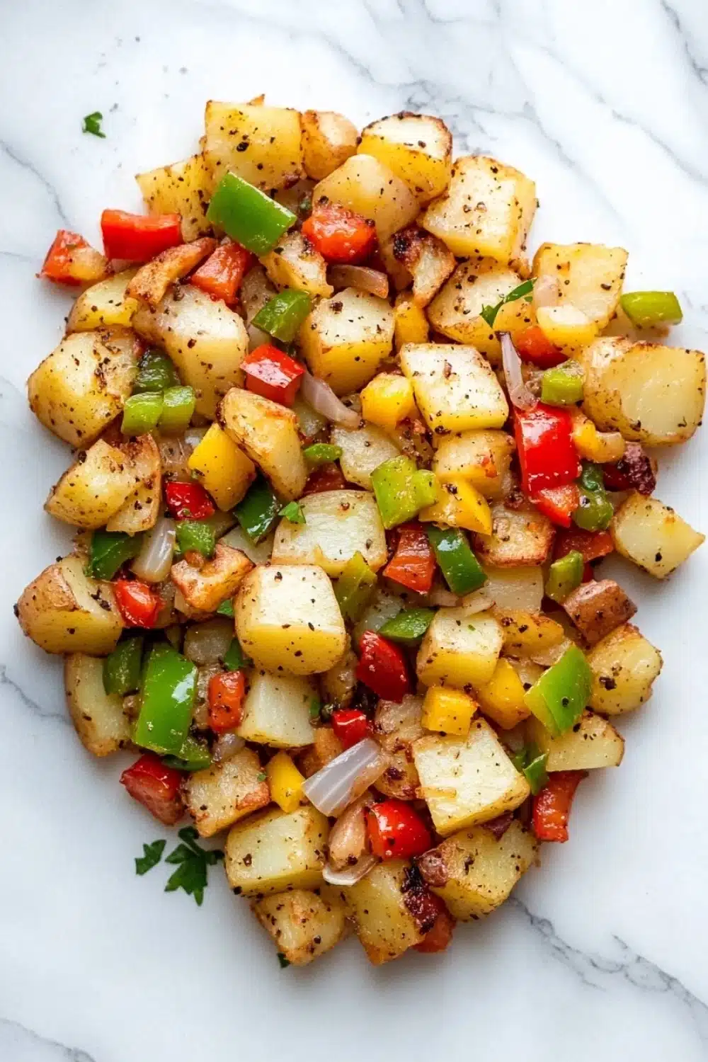 Air fryer potato hash - the image shows a pile of diced potatoes on a white marble countertop. the potatoes are golden brown and appear to be seasoned with herbs and spices. there are also small pieces of red and green bell peppers scattered throughout the dish. the dish is garnished with chopped parsley. the overall appearance of the dish is colorful and appetizing.