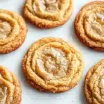 Chewy honey cookie - the image shows a group of freshly baked cookies on a white baking sheet. the cookies are round and golden brown in color, with a swirl pattern on top. they are arranged in a scattered manner, with some overlapping each other. some of the cookies have a light dusting of powdered sugar on top, giving them a shiny appearance. the background is blurred, making the cookies the focal point of the image.