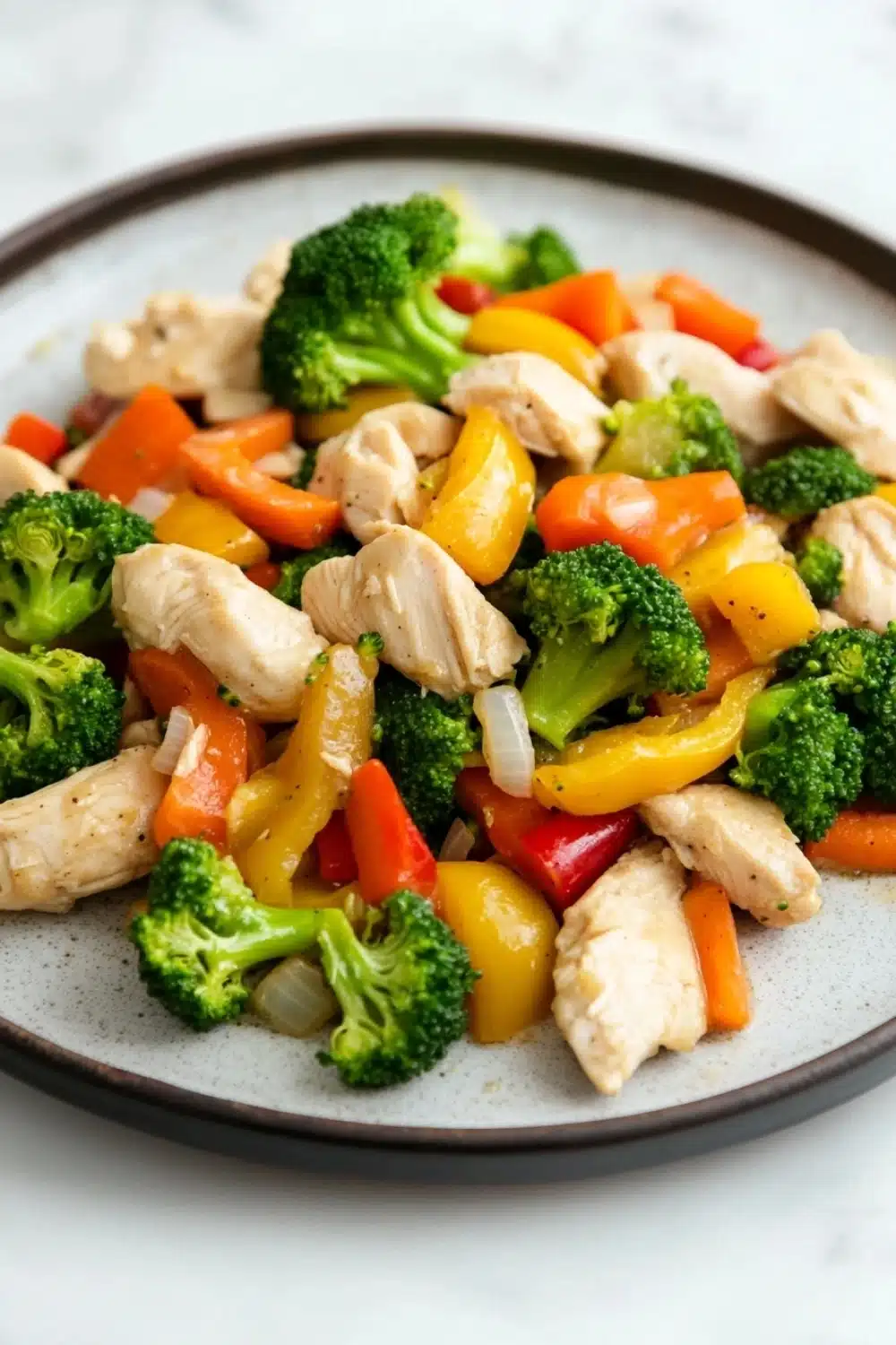 Chicken and vegetables freezer meal - the image is a close-up of a plate of stir-fry with chicken and vegetables. the plate is round and has a gray rim. the chicken is cut into small pieces and is mixed with various vegetables such as broccoli, red and yellow bell peppers, and orange carrots. the vegetables are cut into thin strips and are arranged in a colorful and appetizing manner. the dish appears to be freshly cooked and ready to eat.