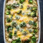 Chicken broccoli casserole with orzo - the image shows a white rectangular baking dish filled with a casserole dish. the dish appears to be made with pasta and broccoli, and it is topped with melted cheese and grated parmesan cheese. the pasta is long and thin, and the broccoli is bright green. the cheese is melted and bubbly, and there are small pieces of broccoli scattered throughout the dish. it looks like it has been cooked and ready to be served. the baking dish is sitting on a wooden table with a rustic background.