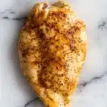 Crock pot chicken breast - the image shows a whole chicken breast on a white marble surface. the chicken breast is golden brown and appears to be seasoned with herbs and spices. the skin of the chicken is slightly charred and has a crispy texture. the herbs are scattered across the surface, giving the chicken a savory flavor. the marble surface has a smooth and polished finish.
