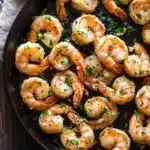 Garlic shrimp in cast iron skillet - the image shows a black cast iron skillet filled with cooked shrimp. the shrimp are orange in color and appear to be seasoned with herbs and spices. the skillet is sitting on a wooden table with a beige cloth napkin on the side. there are a few sprigs of parsley scattered around the skillet. the overall appearance of the dish is appetizing and ready to eat.