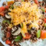 Ground beef dinner make ahead - the image is a close-up of a plate of food. the plate is white and round, and it is placed on a wooden table. the food appears to be a casserole dish with a layer of ground beef, diced tomatoes, green bell peppers, and sliced mushrooms. the beef is cooked to a golden brown color and is topped with melted cheese. the cheese is melted and bubbly, and there are small black pepper sprinkled on top. the dish looks freshly cooked and ready to eat.