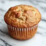 Kodiak muffin mix with yogurt - the image is a close-up of a freshly baked muffin on a white marble countertop. the muffin is golden brown in color and has a crumbly texture on top. it appears to be freshly baked and is sitting on a wooden surface with a black and white marble pattern. the background is blurred, making the muffin the focal point of the image.