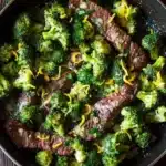 Lemon garlic butter steak and broccoli skillet - the image shows a black frying pan with a serving of cooked beef and broccoli in it. the beef appears to be medium-rare and has a pinkish-brown color. the broccoli is bright green and looks fresh and healthy. the pan is sitting on a wooden table with a few sprigs of parsley scattered around it. there is also a white napkin on the side of the pan. the overall appearance of the dish is savory and appetizing.