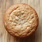 Protein muffin almond flour - the image is a close-up of a round, golden-brown muffin on a wooden surface. the muffin appears to be freshly baked and has a soft, fluffy texture. it is filled with small, white nuts, which are scattered throughout the surface, giving it a crunchy appearance. the background is blurred, making the muffin the focal point of the image.