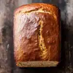 Pumpkin bread almond flour - the image is a close-up of a loaf of bread on a wooden surface. the bread appears to be freshly baked and has a golden brown crust on top. the inside of the bread is visible, with a slice cut out of it, revealing the soft, fluffy interior. the loaf is resting on a dark, textured surface, possibly a table or countertop. the overall mood of the image is rustic and cozy.