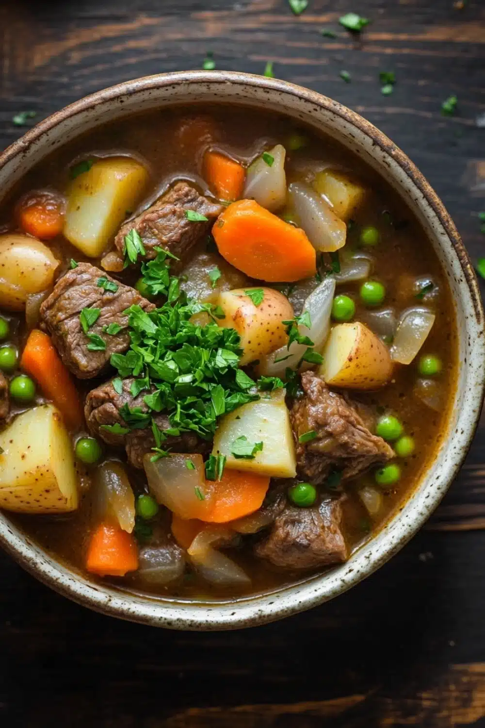 Slow cooker old fashion beef stew - the image is a close-up of a bowl of beef stew. the stew is made with chunks of beef, potatoes, carrots, peas, and onions. the beef is cooked medium-rare and appears to be tender and juicy. the potatoes are cut into small cubes and are scattered throughout the stew. there is a sprig of fresh parsley on top of the stew, adding a pop of green color to the dish. the bowl is made of ceramic and is sitting on a wooden table.