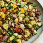 Beef and zucchini skillet - the image is a close-up of a plate of food. the plate is round and has a light blue speckled pattern. the food appears to be a salad with a variety of vegetables, including zucchini, yellow squash, red bell peppers, and onions. the vegetables are arranged in a colorful and appetizing manner, with some overlapping each other. the ground beef is visible in the center of the plate, and it is mixed with the vegetables. there are also some herbs and spices scattered throughout the dish, adding a pop of green color to the dish.