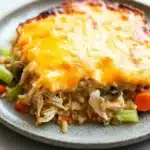Chicken and brown rice casserole - the image shows a plate of food with a slice of chicken pot pie on it. the pie has a golden brown crust on top and is covered in melted cheese. the chicken is cooked until it is golden brown and appears to be seasoned with herbs and spices. the dish is garnished with sliced carrots, celery, and mushrooms. the plate is white with a speckled pattern and is sitting on a white marble countertop.