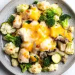 Chicken casserole low carb - the image is a close-up of a plate of food. the plate is gray and has a textured surface. the food appears to be a stir-fry with broccoli, cauliflower, and mushrooms. the broccoli is bright green and the cauliflower is white. the mushrooms are dark brown and are scattered throughout the dish. the cheese is melted and bubbly on top of the vegetables. the dish looks appetizing and ready to eat.