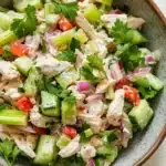 Chicken salad finely chopped - the image is a close-up of a bowl of salad. the bowl is made of ceramic and has a light brown color. the salad is made up of diced celery, red onions, and chunks of chicken. the chicken is mixed with the vegetables, creating a colorful and appetizing appearance. there are also some fresh cilantro leaves scattered throughout the salad, adding a pop of green color to the dish.