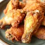 Crispy chicken wings fried - the image shows a plate of fried chicken wings. the wings are golden brown and appear to be crispy on the outside. they are arranged in a circular pattern on the plate, with some overlapping each other. the plate is made of dark green ceramic with a brown rim. the background is white, making the plate and wings the focal point of the image.