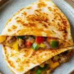 Freezer breakfast quesadilla - the image shows two quesadillas stacked on top of each other on a blue plate. the quesads are golden brown and appear to be freshly cooked. they are filled with ground beef, diced red and green bell peppers, diced onions, and melted cheese. the plate is sitting on a wooden table.