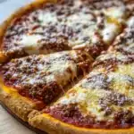 Frozen deep dish pizza - the image shows a large pizza on a wooden cutting board. the pizza has a golden brown crust and is topped with melted cheese and ground meat. the cheese is melted and bubbly, and the meat appears to be ground beef or ground beef. there are also small pieces of pepperoni scattered on top of the cheese. the cutting board is placed on a white wooden table, and there is a black cup of coffee in the background.
