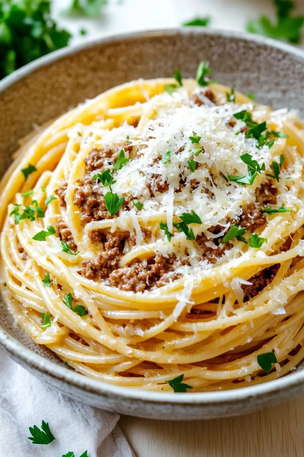 One pot garlic butter pasta with beef - the image is a close-up of a plate of spaghetti bolognese. the spaghetti is cooked al dente and is topped with a generous amount of minced meat and grated parmesan cheese. the dish is garnished with fresh parsley leaves. the plate is sitting on a wooden table with a white napkin underneath. the background is blurred, but it appears to be a kitchen countertop.