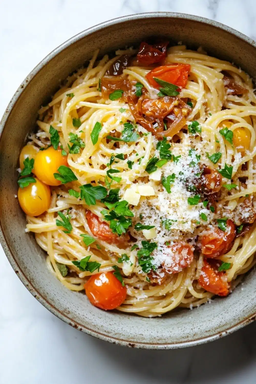 One pot pasta zwiebel - the image is a close-up of a bowl of spaghetti dish. the spaghetti is cooked al dente and is topped with chunks of tomato sauce, sliced onions, and grated parmesan cheese. the dish is garnished with fresh parsley and cherry tomatoes. the bowl is made of ceramic and is sitting on a white marble countertop. the overall color scheme of the dish is warm and inviting.