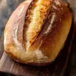 Red star rise yeast bread - the image is a close-up of a freshly baked loaf of bread on a wooden cutting board. the bread is golden brown in color and has a soft, fluffy texture. it appears to be freshly baked, with a slightly crisp crust on top and a soft soft interior. the loaf is resting on a dark wooden surface, and the background is blurred, making the bread the focal point of the image.