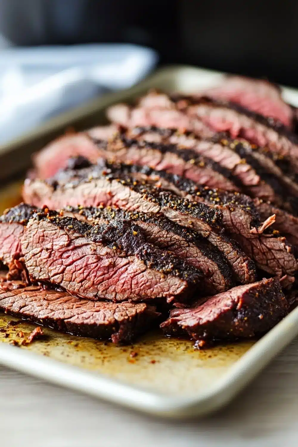 Slow cooker deli roast beef - the image shows a plate of sliced steak on a white rectangular plate. the steak appears to be cooked medium-rare, with a pinkish-red color and a slightly charred texture. the slices are arranged in a single layer on the plate, with some overlapping each other. the plate is sitting on a wooden table, and there is a white napkin on the side. the background is blurred, but it seems to be a kitchen countertop.