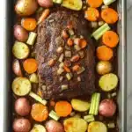 Slow cooker pot roast and vegetables - the image shows a rectangular baking dish filled with a roast beef dish. the roast beef is cooked medium-rare and is garnished with chopped carrots, celery, and onions. the dish is served in a black baking tray with a white marble countertop. there are also small potatoes and carrots scattered throughout the dish, adding a pop of color and texture. the overall appearance of the dish is savory and appetizing.