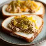 Tuna melt with relish - the image shows two slices of bread on a blue and white plate. the bread appears to be toasted and has a golden brown crust. on top of the bread, there is a mixture of ground meat, possibly tuna or tuna, with a dollop of green sauce on top. the sauce is drizzled over the top, giving it a glossy sheen. the plate is sitting on a white tablecloth.