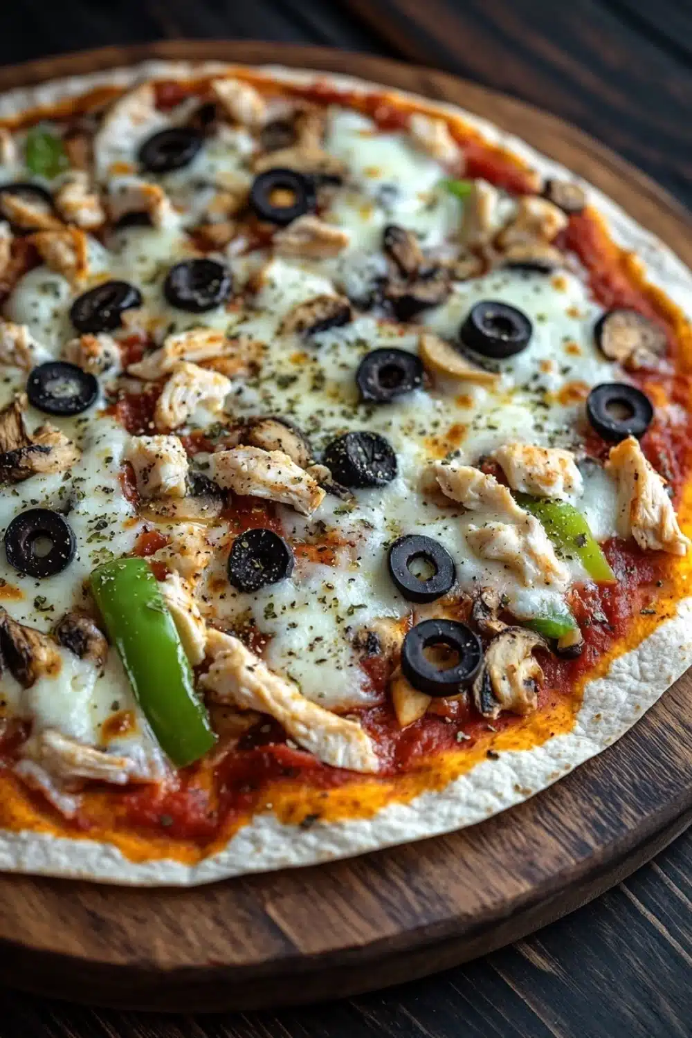 Air fryer deep dish tortilla pizza - the image is a close-up of a pizza on a wooden cutting board. the pizza is topped with melted cheese, sliced mushrooms, black olives, and green bell peppers. the cheese is melted and bubbly, and the toppings are arranged in a circular pattern around the edges of the pizza. the background is dark, making the pizza stand out.