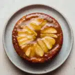 Apple cake glaze - the image is a close-up of a round cake on a light blue plate. the cake appears to be a tart or a dessert, with a golden brown crust and a layer of caramel sauce on top. the caramel sauce is drizzled over the top of the cake, creating a swirl pattern. there are several slices of caramel arranged in a circular pattern on the cake. the plate is sitting on a white countertop.
