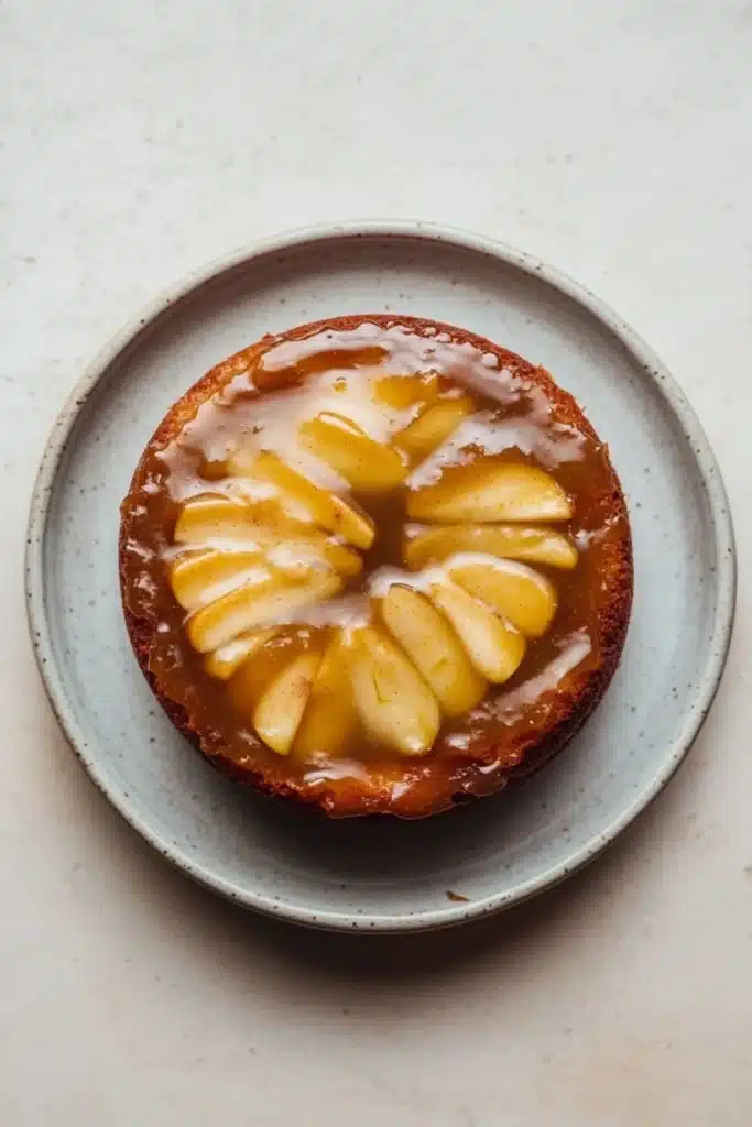 Apple cake glaze - the image is a close-up of a round cake on a light blue plate. the cake appears to be a tart or a dessert, with a golden brown crust and a layer of caramel sauce on top. the caramel sauce is drizzled over the top of the cake, creating a swirl pattern. there are several slices of caramel arranged in a circular pattern on the cake. the plate is sitting on a white countertop.