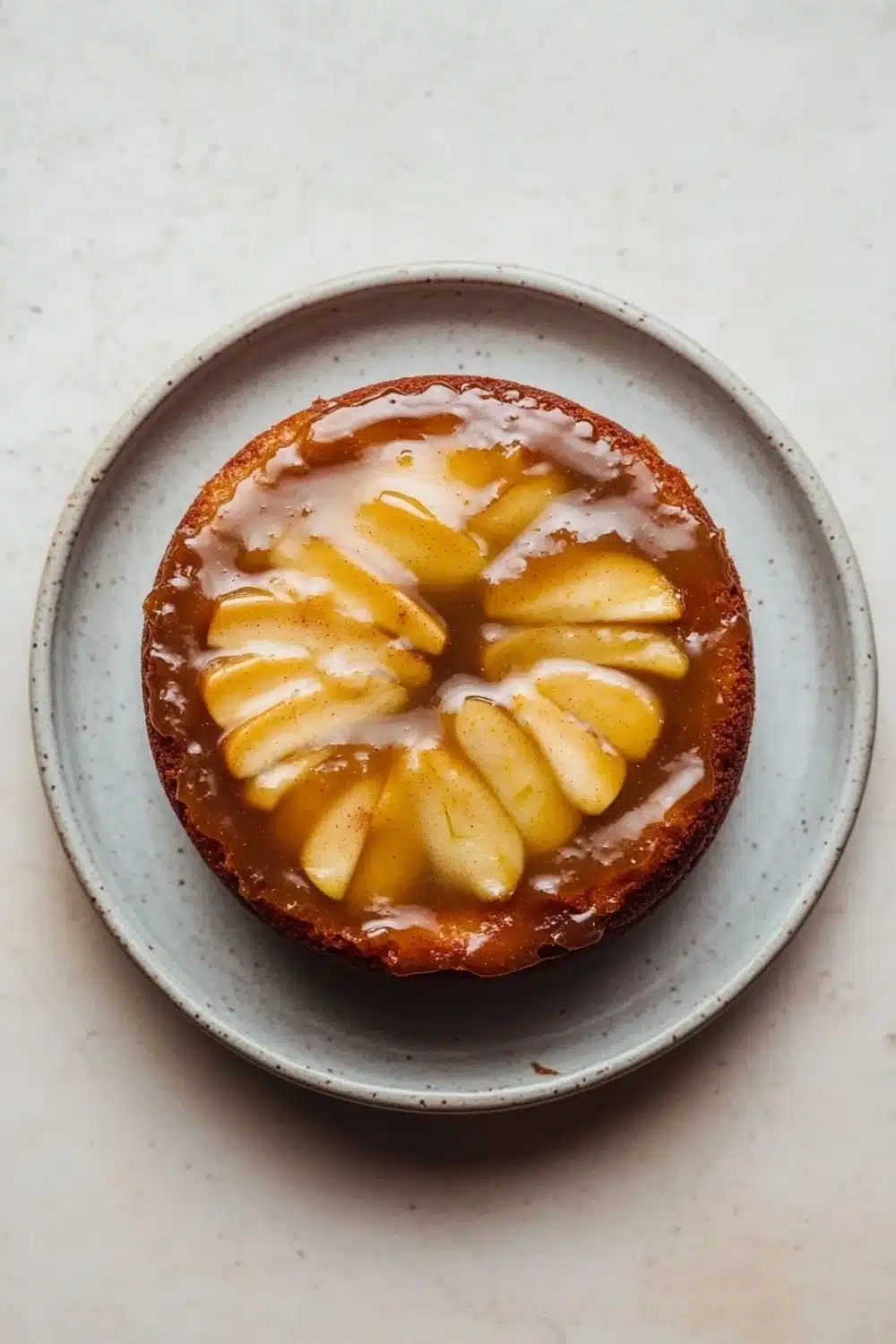 Apple cake glaze - the image is a close-up of a round cake on a light blue plate. the cake appears to be a tart or a dessert, with a golden brown crust and a layer of caramel sauce on top. the caramel sauce is drizzled over the top of the cake, creating a swirl pattern. there are several slices of caramel arranged in a circular pattern on the cake. the plate is sitting on a white countertop.