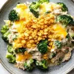 Chicken broccoli casserole cream of mushroom - the image is a close-up of a dish in a gray bowl. the dish appears to be a casserole or pasta dish with a creamy white sauce and chunks of chicken and broccoli mixed in. the top of the dish is covered in a layer of melted cheese, which is golden brown and bubbly. the broccoli is bright green and looks fresh and healthy. the bowl is sitting on a white marble countertop.