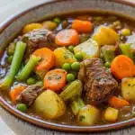 Freezer vegetable beef stew - the image is a close-up of a bowl of beef stew. the stew is made with chunks of beef, carrots, celery, and potatoes. the beef is cooked medium-rare and appears to be tender and juicy. the vegetables are mixed in with the stew, creating a colorful and flavorful dish. the bowl is made of ceramic and is sitting on a wooden table. the background is blurred, making the bowl the focal point of the image.