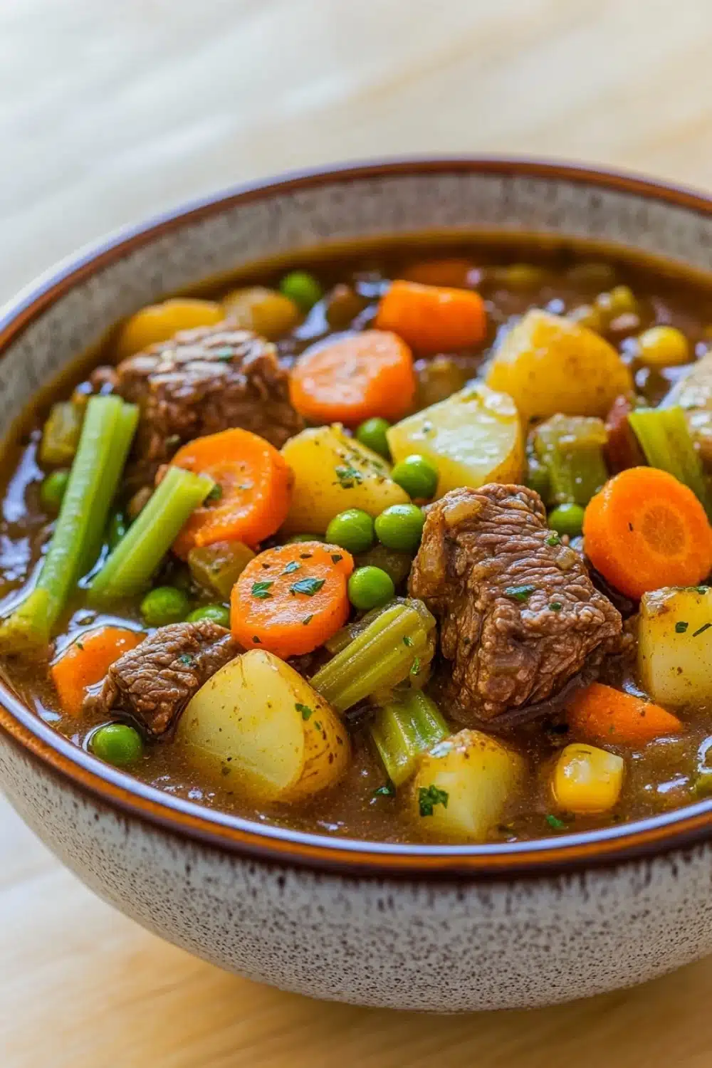 Freezer vegetable beef stew - the image is a close-up of a bowl of beef stew. the stew is made with chunks of beef, carrots, celery, and potatoes. the beef is cooked medium-rare and appears to be tender and juicy. the vegetables are mixed in with the stew, creating a colorful and flavorful dish. the bowl is made of ceramic and is sitting on a wooden table. the background is blurred, making the bowl the focal point of the image.