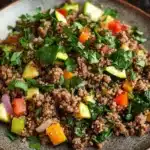 Ground beef dinner high protein - the image is a close-up of a plate of food. the plate is made of dark brown ceramic and is placed on a wooden table. the food appears to be a salad with a variety of ingredients, including quinoa, sliced zucchini, red bell peppers, and greens. the quinoa is a light brown color and is mixed with the vegetables, creating a colorful and appetizing dish. the vegetables are arranged in a circular pattern on top of the quinoa. there are also some fresh herbs scattered throughout the dish, adding a pop of green color. the overall appearance of the dish is fresh and vibrant.