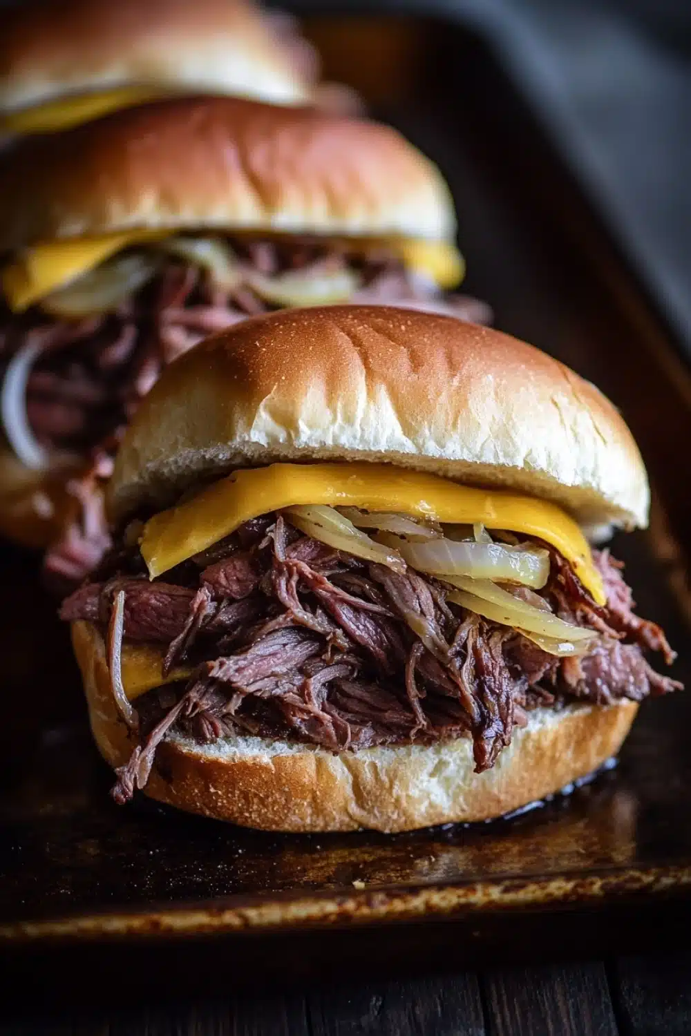 Hot roast beef sandwich slow cooker - the image shows three pulled pork sandwiches on a wooden tray. the sandwiches are made with a toasted bun and are topped with shredded beef, sliced onions, and melted cheese. the beef appears to be cooked medium-rare and the onions are caramelized. the cheese is melted and oozing out of the sides of the sandwiches. the tray is dark and the background is blurred, making the sandwiches the focal point of the image.