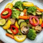 Restaurant style sauteed vegetables - the image is a close-up of a plate of food. the plate is round and has a light blue speckled pattern. the food appears to be a stir-fry dish with various vegetables, including broccoli, zucchini, bell peppers, and mushrooms. the vegetables are cut into small pieces and are arranged in a colorful and appetizing manner. the colors of the vegetables are vibrant and the dish looks fresh and fresh.