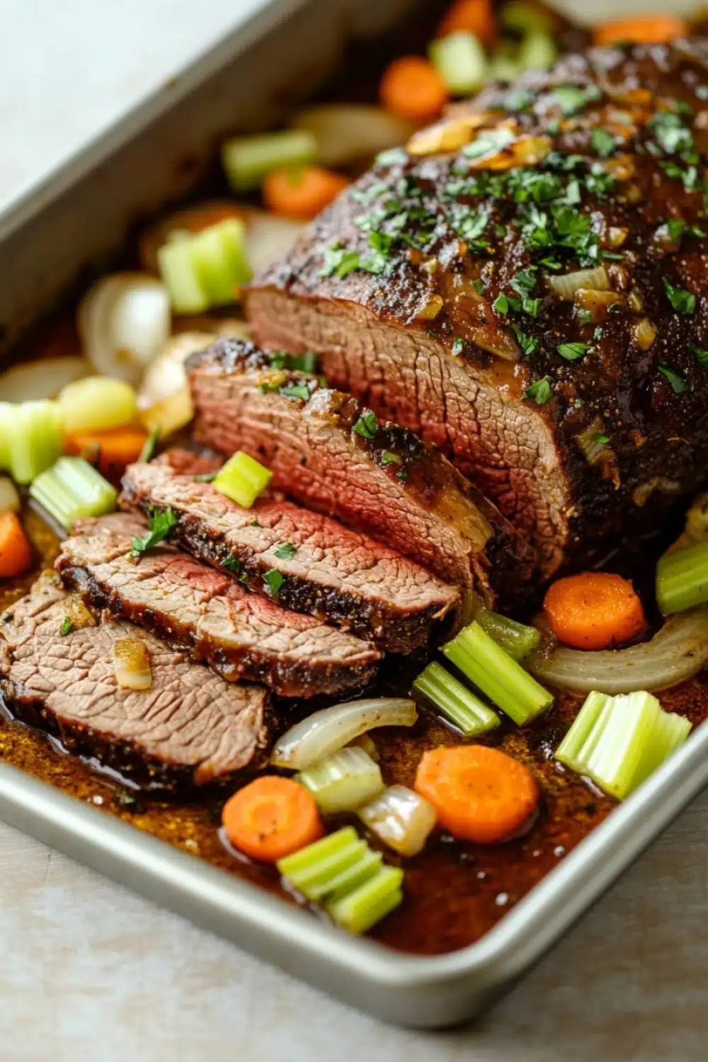 Roast beef marinade slow cooker - the image shows a rectangular baking dish with a large piece of cooked meat on it. the meat appears to be a roast beef, with a dark brown color and a shiny texture. it is garnished with chopped parsley and sliced onions. the dish is served on a bed of sliced carrots and celery, and there is a drizzle of sauce on top. the background is a white countertop.